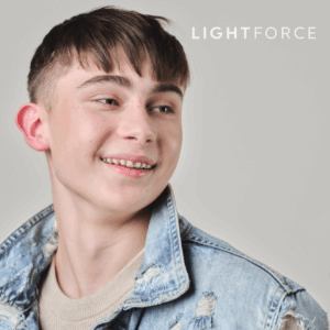 Braces-that-encourage-you-to-stand-out-2-copy-6 Teen boy with braces smiling and looking to the side, wearing a distressed denim jacket and beige shirt. The word "LIGHTFORCE" appears in the top right corner.