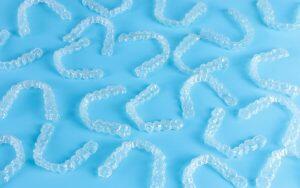A group of clear plastic Invisalign teeth whitening trays on a blue background.