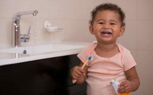 A little girl using a toothbrush in front of a sink, promoting proper oral hygiene.