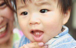 A woman holds a baby while wondering about the timing of baby teeth falling out and how children's primary teeth erupt and fall out.