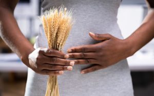 Person holding a bundle of wheat in one hand and touching their abdomen with the other, possibly indicating a stomach concern.